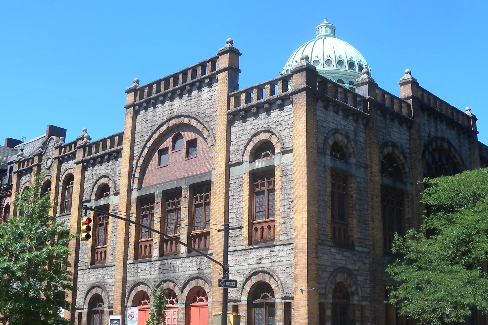 Mount Morris Ascension Presbyterian Church in Harlem, a granite and gold-brick building with a patinated green copper dome, seen from across the street on a sunny day
